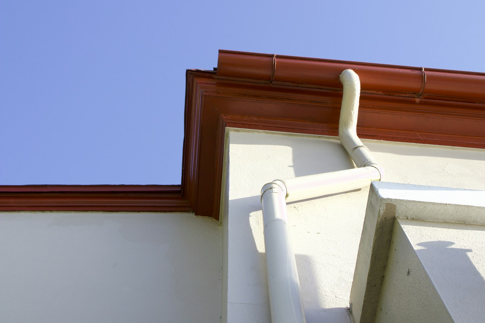 Roof gutter connected to a white downspout on an exterior wall